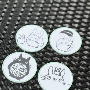 May include: Four circular coasters with a light green border and white center. Each features black line art of characters from My Neighbor Totoro. One coaster displays the text MY NEIGHBOR TOTORO inside a large character silhouette.