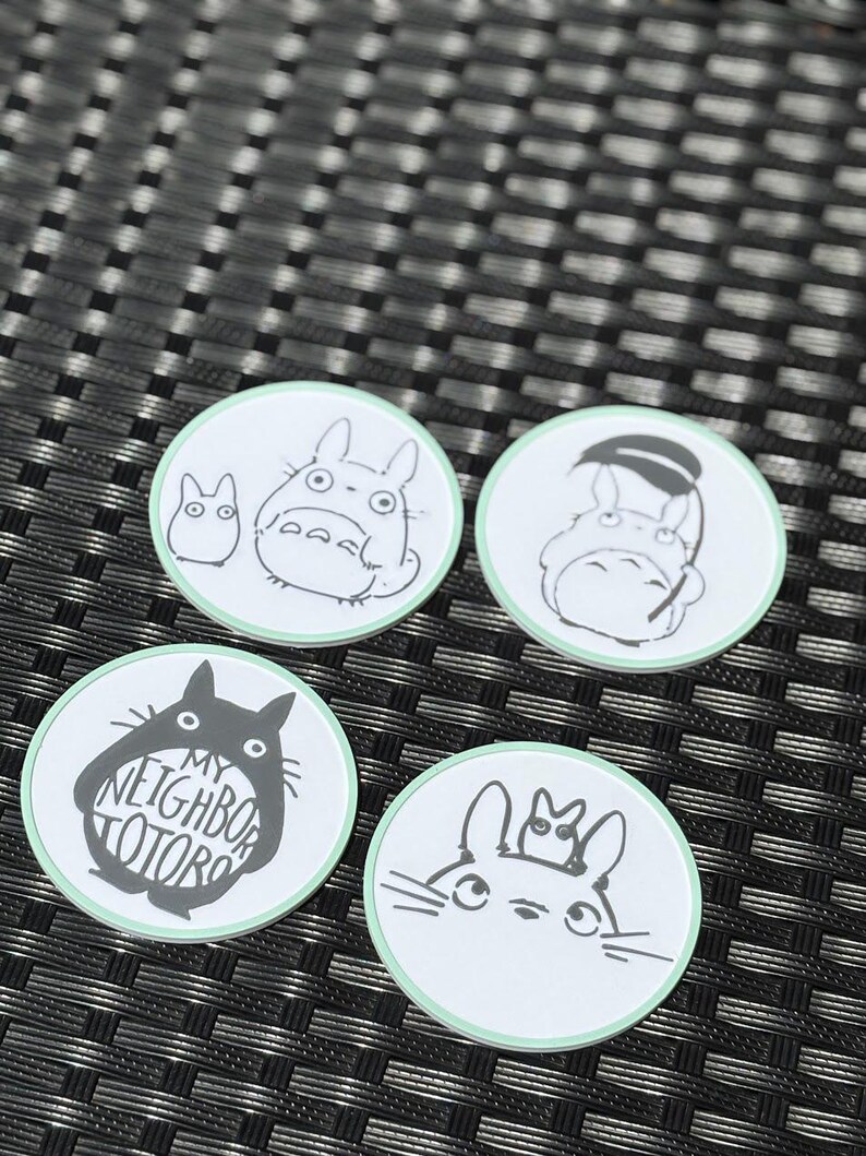 May include: Four circular coasters with a light green border and white center. Each features black line art of characters from My Neighbor Totoro. One coaster displays the text MY NEIGHBOR TOTORO inside a large character silhouette.