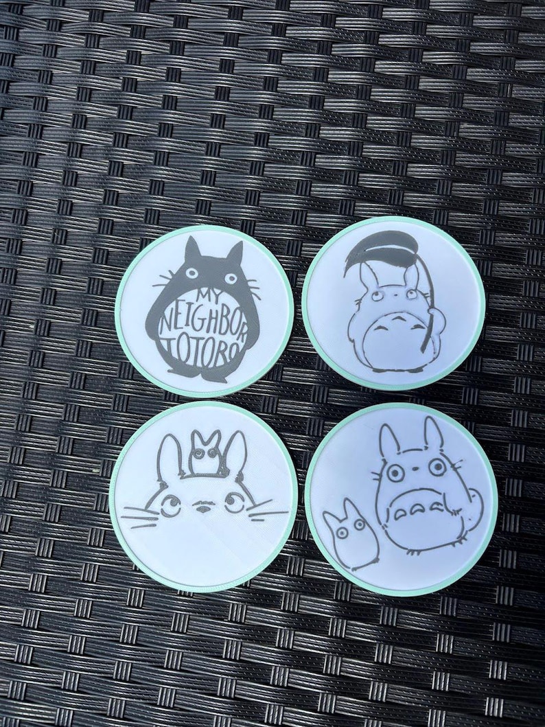 May include: Four circular coasters with a light green border, each featuring a black and white illustration of characters from My Neighbor Totoro. The top left coaster displays the text My Neighbor Totoro inside the silhouette of the large character.