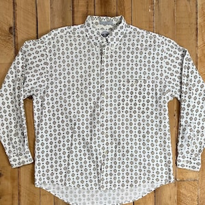 May include: White button-down shirt with a repeating pattern of small brown, gold, and dark green diamond shapes. The long-sleeved shirt has a collar and a single chest pocket.