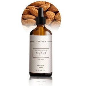 May include: A brown glass bottle with a dropper top filled with almond oil. The label reads "Dan Dur 100% Pure & Organic Almond Oil Cold Pressed Product of India 30 ml / 1.01 fl.oz."