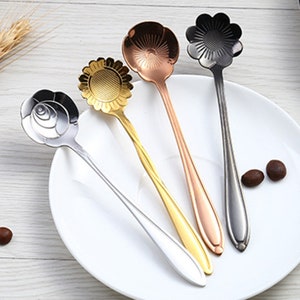 May include: Four decorative spoons with flower-shaped handles. The spoons are made of metal and have different finishes: gold, silver, black, and rose gold.