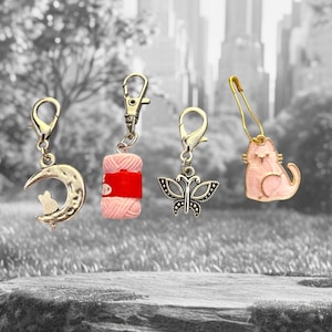 May include: Four silver charms with lobster clasps. One shows a crescent moon with a cat, another a pink yarn ball with a red band, a butterfly, and a pink cat charm on a safety pin. Suitable for crafting or jewellery.