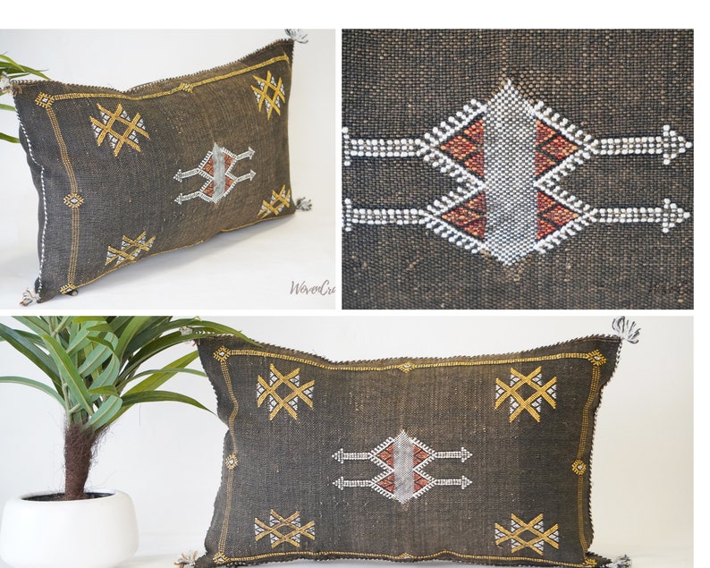 May include: A dark brown throw pillow with a geometric pattern in gold and white. The pillow has a fringe trim and is made of a woven fabric.