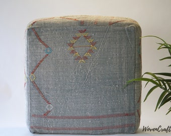 May include: A gray square ottoman with a geometric pattern in red, yellow, blue, and orange. The ottoman is made of woven fabric and has a tufted top.