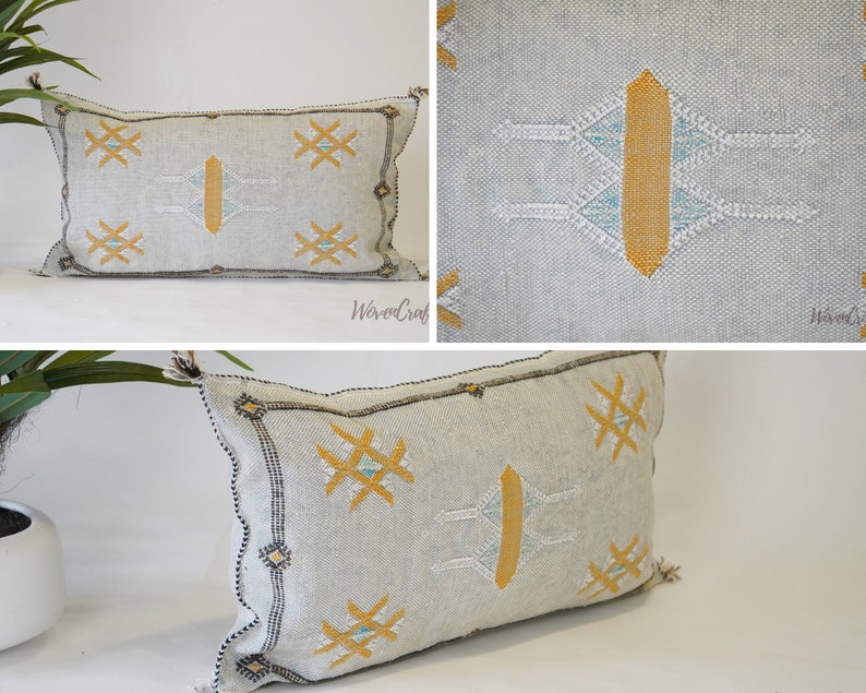 May include: A white and gray rectangular pillow with a geometric pattern in yellow and blue thread. The pillow has a fringe on the edges.