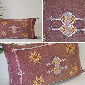 May include: A burgundy throw pillow with a geometric pattern in white and yellow thread. The pillow has a fringe border and is made of a soft, woven fabric.