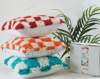 May include: Three decorative throw pillows with a white base and colorful geometric patterns. The pillows are stacked on top of each other, with the red and white pillow on top, the orange and white pillow in the middle, and the turquoise and white pillow on the bottom. The pillows are made of a soft, fluffy material.