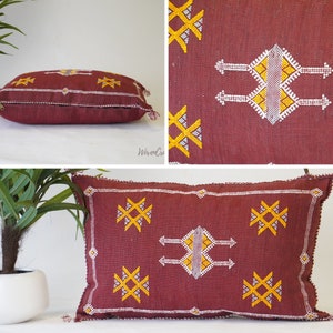 May include: A burgundy throw pillow with a white and yellow geometric pattern. The pillow has a zipper closure and tassels on the corners.
