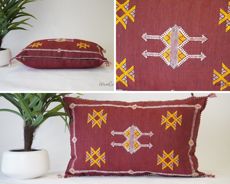 May include: A burgundy throw pillow with a white and yellow geometric pattern. The pillow has a zipper closure and tassels on the corners.