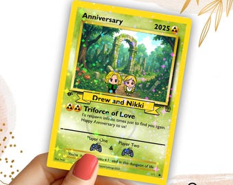 May include: A custom anniversary card with a yellow border, featuring a forest scene with two cartoon figures. The card reads "Anniversary 2025", "Drew and Nikki", and "Triforce of Love". The card is held by a person with red nail polish.