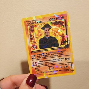 May include: A graduation card designed to look like a Pokemon card. The card features a photo of a graduate in a cap and gown, and the text "Graduating Pokemon Richard Voga 2022 HP". The card also includes the text "Congratulations! Your journey was never easy but your hard work paid off! Class of 2022!" and "Diploma This card certifies that Richard has passed the test by Professor Oak to become a 2022 graduate!!"