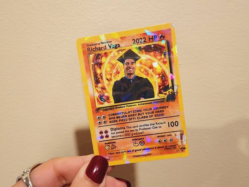 May include: A graduation card designed to look like a Pokemon card. The card features a photo of a graduate in a cap and gown, and the text "Graduating Pokemon Richard Voga 2022 HP". The card also includes the text "Congratulations! Your journey was never easy but your hard work paid off! Class of 2022!" and "Diploma This card certifies that Richard has passed the test by Professor Oak to become a 2022 graduate!!"
