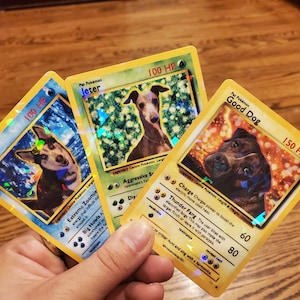 May include: Three Pokemon cards featuring dogs. The cards are yellow with holographic accents. The first card features a black and white dog with blue eyes and the text "Zelda 100 HP". The second card features a brown and white dog with the text "Jeter 100 HP". The third card features a brown dog with the text "Good Dog 150 HP".