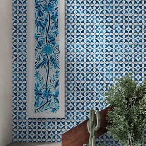 Puede incluir: Una pieza de arte mural rectangular vertical que presenta una ilustración de arte popular en azul y blanco de aves, flores y follaje, exhibida en una pared cubierta con un patrón geométrico circular azul y blanco sobre escaleras de concreto.
