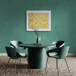 May include: A round dark green dining table with four matching curved chairs. On the table sits a small gray vase with a sprig of greenery and a white candle. A framed square print with a yellow pattern of birds and rabbits hangs above.