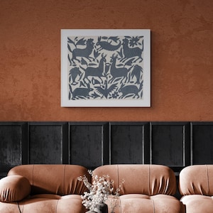Puede incluir: Una pieza de arte mural cuadrada enmarcada que presenta un fondo de color crema con un patrón repetitivo de color azul oscuro de animales estilizados, incluyendo ciervos, conejos y aves, intercalados con motivos florales y de hojas en una disposición simétrica.