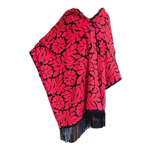 May include: A red and black poncho with a floral pattern and fringe. The poncho is made of a soft, lightweight fabric and is perfect for layering.