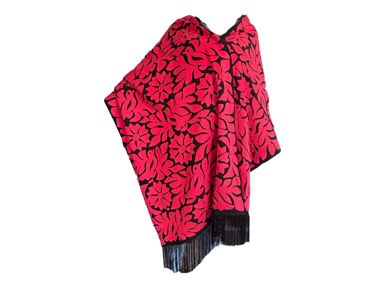 May include: A red and black poncho with a floral pattern and fringe. The poncho is made of a soft, lightweight fabric and is perfect for layering.