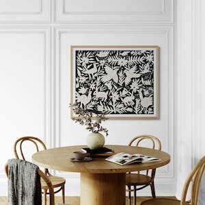 May include: A round wooden dining table with a central pedestal base, surrounded by four light-colored rattan chairs. A gray throw blanket hangs over one chair. On the table sits a ceramic vase with branches, a cup, and an open magazine.