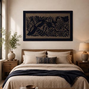 May include: A rectangular wall hanging featuring a dark navy blue embroidered design of birds and foliage on a tan fabric background, framed by a solid navy blue border. The artwork is displayed horizontally above a bed with neutral bedding.