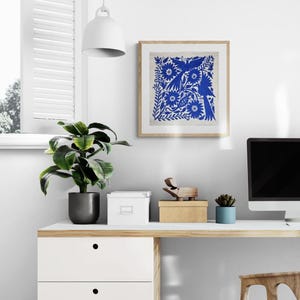May include: A square framed wall art piece featuring a vibrant blue intricate folk-style pattern of birds and flowers on a light background. The artwork is displayed in a light-colored wooden frame, showcasing detailed botanical and avian motifs.