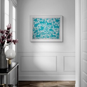 May include: A rectangular wall art print featuring a repeating pattern of turquoise blue rabbits, birds, and floral motifs on a light gray background, enclosed in a simple white frame and mounted on a white wall with wainscoting.