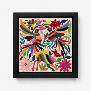 Puede incluir: Un marco cuadrado negro que contiene una pieza de tela color hueso con bordado a mano colorido. El diseño presenta dos pájaros y un animal de cuatro patas rodeados por varias flores y hojas estilizadas en tonos vibrantes de rojo, azul, naranja, verde, morado y rosa.