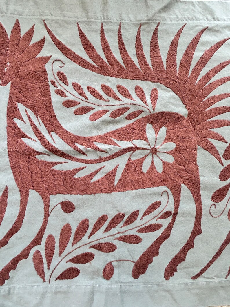 May include: A light gray fabric textile featuring intricate dark brown embroidery of a stylized mythical creature with a long neck, feathered wings, and a tail. The design includes floral and leaf motifs integrated into the creature's body.