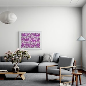 May include: A rectangular wall art print featuring a vibrant purple folk-art style pattern of stylized birds, deer, and floral motifs on a light background, displayed in a simple white frame hanging on a plain wall above a gray sofa.