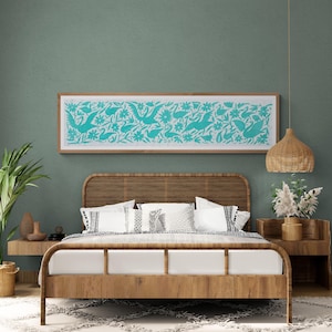 Puede incluir: Una pieza de arte mural rectangular que presenta un estampado turquesa vibrante de aves y flores sobre un fondo blanco, encerrada en un marco de madera clara. La obra se exhibe horizontalmente sobre una cama de madera con cabecero de rejilla.
