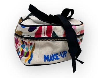 May include: A white canvas makeup bag with a black zipper and a black ribbon handle. The bag is embroidered with colorful flowers and the words "MAKE-UP" in blue.