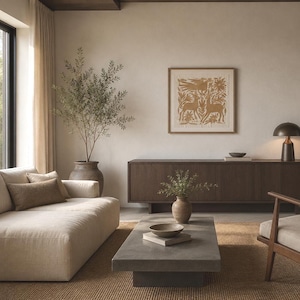 May include: A living room featuring a beige sofa with a rectangular pillow, a low gray concrete coffee table with a bowl on a book, a dark wood sideboard, a framed square print with gold animal illustrations, and a tall potted olive tree.