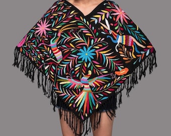 May include: A black poncho featuring vibrant, multi-colored floral and animal embroidery. The garment has a V-neckline and is finished with long black fringe along the bottom edges, creating a triangular silhouette with intricate, colorful patterns.