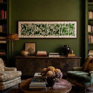 May include: A living room featuring two upholstered armchairs, a dark wooden sideboard, and a round coffee table with a vase of dried flowers and stacked books. A long rectangular wall art piece with green nature-themed patterns hangs above.