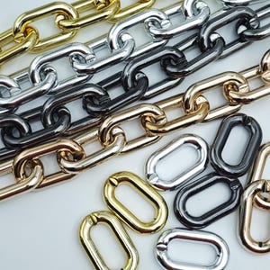 Könnte beinhalten: Nahaufnahme verschiedener Metallketten in Gold, Silber und Schwarz. Die Ketten sind in Reihen angeordnet und verstreut, wobei ihre verschiedenen Farben und Texturen zur Geltung kommen. Die Glieder sind oval geformt und haben eine glänzende Oberfläche.