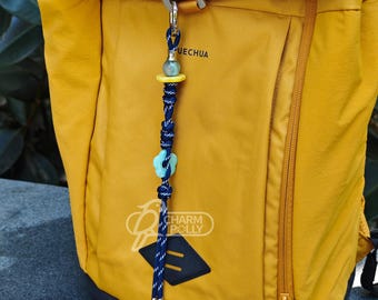 May include: A decorative charm with a blue and white braided cord, a light blue flower, and a yellow bead, attached to a yellow backpack. The charm has a silver clasp and the text "CHARM POLLY".