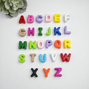 Peut inclure: Un ensemble de lettres de l'alphabet colorées, dans des tons variés comme le rouge, le rose et le vert. Les lettres sont disposées en rangées, chacune étant clairement visible. Les lettres sont en matériau brillant.