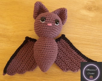 May include: A crocheted purple bat with black trim on the wings. The bat has large black eyes and a pink nose.