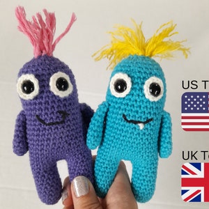 May include: Two crocheted amigurumi monsters, one purple with pink hair and one blue with yellow hair. Both have white eyes and a smiling mouth.
