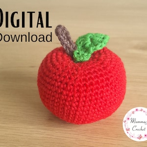 Peut inclure: Une pomme rouge crochetée à la main, avec une feuille verte et une tige marron. Le texte « DIGITAL Download » est visible. L'objet est posé sur une surface en bois.