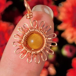 May include: A copper wire wrapped sunflower pendant with a golden tiger's eye stone in the center.