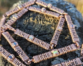 May include: Two copper wire wrapped bracelets with opal stones. The bracelets are woven in a square pattern and are stacked on top of each other.