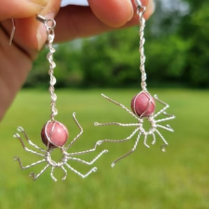 May include: A pair of silver wire earrings with pink gemstone spider accents.