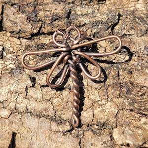 May include: A copper wire dragonfly pendant with a twisted tail. The dragonfly is made of wire and has a delicate, intricate design.