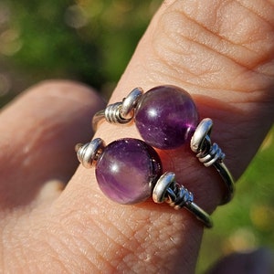 May include: A silver wire wrapped ring with two amethyst stones. The stones are round and purple.