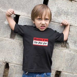 Puede incluir: Un niño pequeño con una camiseta negra con una etiqueta de nombre roja y blanca que dice "Hello I'm The Bad Guy".