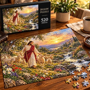 Könnte beinhalten: Ein 520-Teile-Puzzle mit einer Landschaftsillustration einer Figur in weißem Gewand und roter Schärpe, die mit einer Schafherde an einem Bach entlanggeht. Die Schachtel zeigt den Text JIGSAW PUZZLE 520 PIECES und das gleiche Motiv.