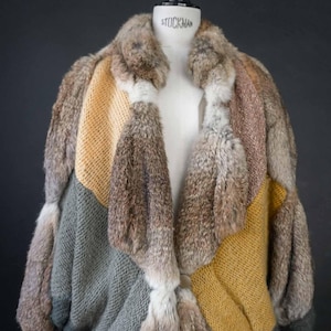 Könnte beinhalten: Ein Patchwork-Mantel mit einem Mix aus Texturen und Farben. Der Mantel hat Abschnitte aus Strickstoff in Grau und Senfgelb, kombiniert mit Pelzbahnen in Braun und Grau. Der Mantel wird auf einer Schaufensterpuppe präsentiert.