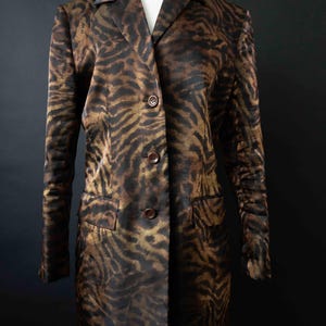 Op de afbeelding: Een lange blazer met knopen en een bruin-zwarte dierenprint. De blazer heeft een reverskraag, twee voorzakken en drie knopen aan de voorkant. Het kledingstuk wordt op een mannequin gepresenteerd.
